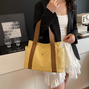 Detail view of yellow canvas tote bag with brown fabric handle and side pocket feature