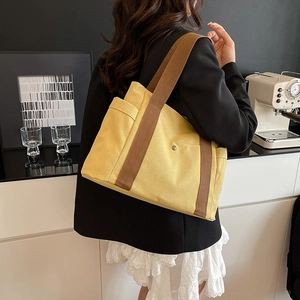 Detail view of mustard yellow canvas tote bag with brown straps in a lifestyle setting