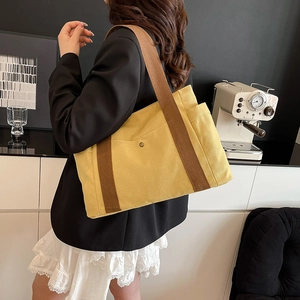 Detail view of yellow canvas tote bag with wide brown strap and stylish snap button