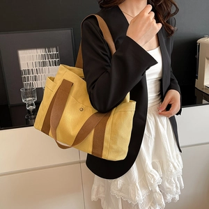 Detail of yellow canvas tote bag with brown straps styled on a female model with black suit