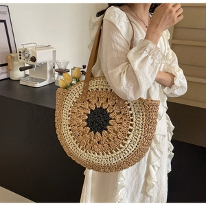 Close-up of a sunflower-shaped straw tote bag with brown leather handles worn by a model