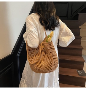 Close-up of a large hollow woven tote bag in brown displayed by a model in a white dress