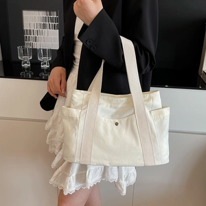 Detail of canvas tote bag with side pockets and woven handles worn with black blazer
