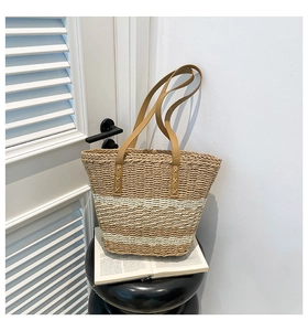 Detailed view of the woven straw tote bag with brown leather handles and cross-stitch detail