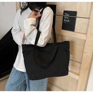 Detail view of a large black canvas tote bag with wide straps and functional side pockets