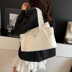 Detail of off-white canvas tote bag with side pockets and a vintage metal snap button