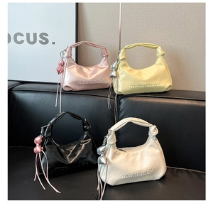 Quatre sacs demi-lune colorés avec logo embossé disposés sur un canapé en cuir noir