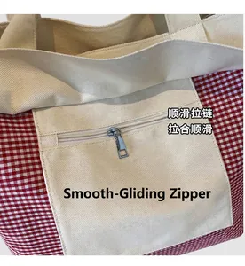 Detailed close-up of smooth silver metal zipper on red and white checkered canvas tote bag