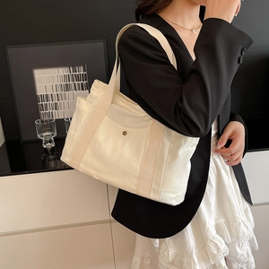 Model wearing off-white canvas tote bag with side pockets in a minimalist interior