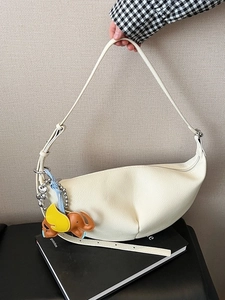 Cream leather croissant bag with pebble texture and elephant charm hand-held view
