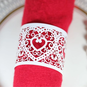 White laser-cut heart napkin ring with ornate hollow patterns on a red cloth napkin