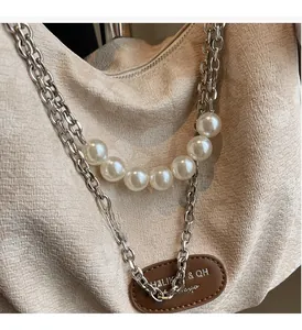 Detail of beige canvas tote with decorative silver chain, pearls, and brown leather tag