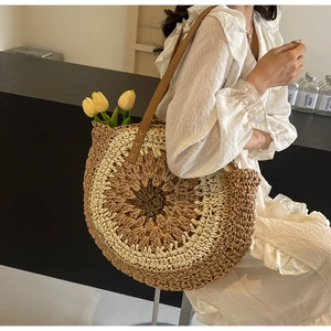 Detail of round straw tote bag with brown leather strap and intricate woven texture