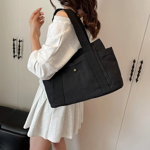 Close-up of black canvas tote bag with side pocket and metal snap button detail
