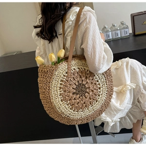 Detailed view of a circular woven straw tote bag with brown leather straps on a model