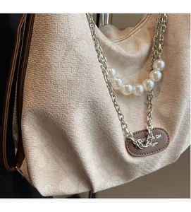 Detail of beige textured fabric shoulder bag with pearl chain and leather logo patch
