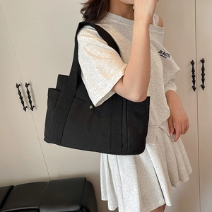Detail view of black canvas tote bag with side pocket and snap button on a model