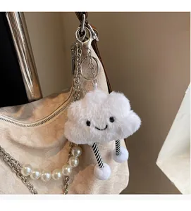 Close-up of fluffy white cloud keychain with smiley face hanging on a beige handbag