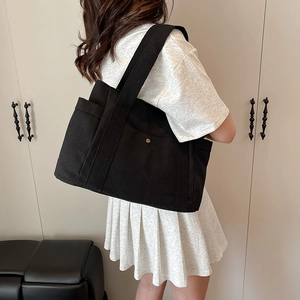 Detail of black canvas tote bag showing wide shoulder strap and metal buckle accents