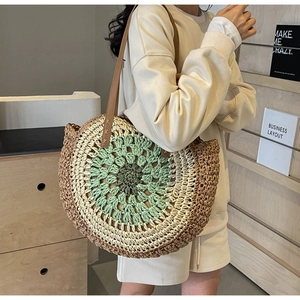 Detail of a large circular woven tote bag with leather straps and colorful straw patterns