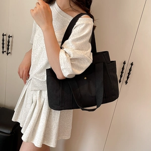 Detail of a black canvas tote bag with multiple pockets and bronze snap button closure