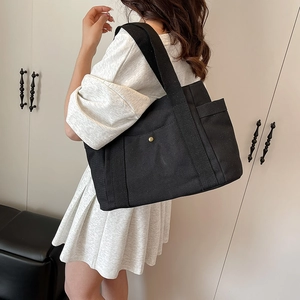 Close-up of black high-density canvas tote bag with side pocket and gold snap button detail