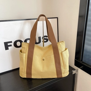 Detail of yellow canvas tote bag with brown fabric strap and front pocket with snap button