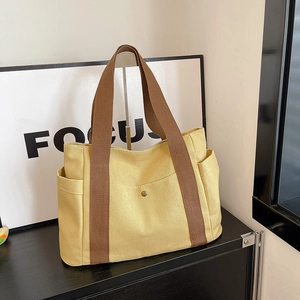 Detail view of canvas tote bag showing side pocket and dark brown woven straps