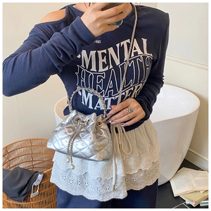 Close-up of silver quilted bucket bag featuring chain handle and pearl drawstring charms