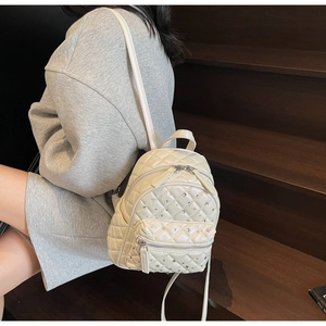 Detail of white quilted mini backpack with pearl finish and rhinestone accents on stairs