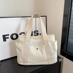 Detail of off-white canvas tote bag with metal buckle pocket and reinforced wide strap