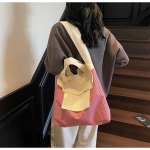 Detail view of large red plaid canvas tote bag worn by model in a casual staircase setting