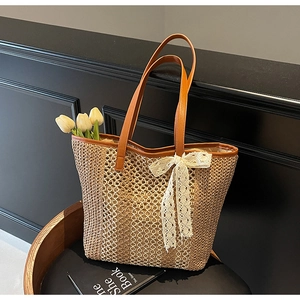 Détail du sac cabas en paille tissée avec nœud en dentelle et poignée en cuir brun