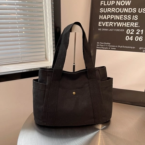Detail of a black canvas tote bag showing side pockets and metal snap fastener detail