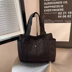 Detail of black canvas tote bag with deep front pocket and bronze button on a metal table