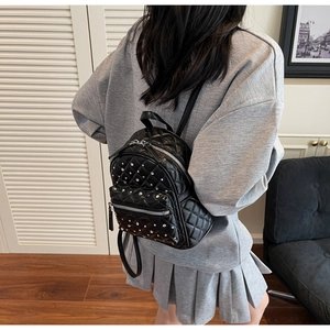 Detail of black quilted mini backpack with silver studs worn by a model in a home setting