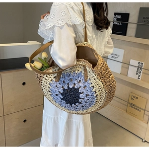 Detail of woven straw tote bag featuring blue sunflower embroidery and brown leather straps