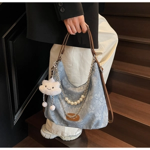 Detailed view of denim floral tote bag with pearl chain and cloud plush charm detail