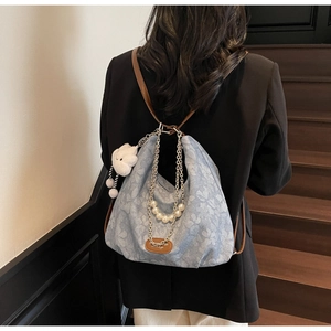 Detail of light blue floral denim backpack with silver chain and white plush charm