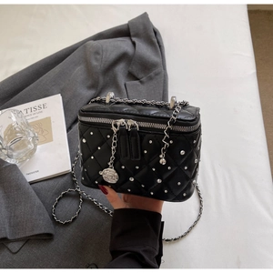 Detail of black quilted box bag with silver studs, dual zippers and floral chain charm