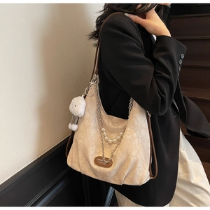 Detail view of beige canvas hobo bag with pearl chain, leather logo and plush charm