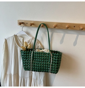 Detail van donkergroene gevlochten tas met witte trekkoordsluiting tegen lichte achtergrond