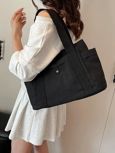 Minimalist black canvas tote bag with gold buckle and wide shoulder strap for commuting