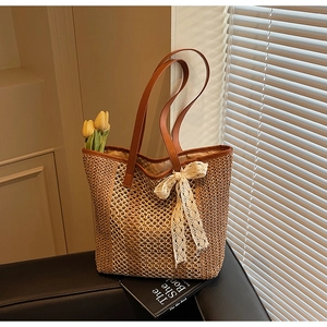 Détail du sac cabas en paille tissée avec anses en cuir marron et nœud en dentelle