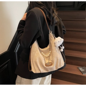 Detail of cream tote bag featuring pearl chain and plush cloud charm on a wooden staircase