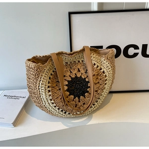 Handmade woven straw tote bag with sunflower pattern and leather handles on white table