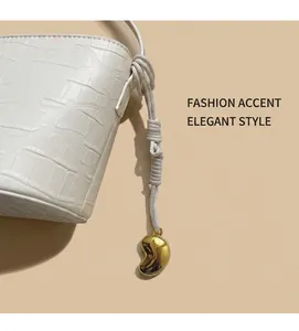 Detail of white crocodile pattern bucket bag with braided rope strap and gold charm