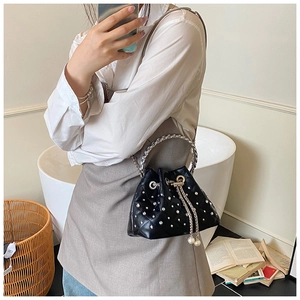Close-up of black quilted bucket bag with white rhinestones and pearl chain detail