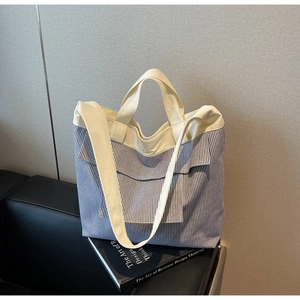 Detail of blue striped canvas tote bag with off-white handles on a black leather sofa