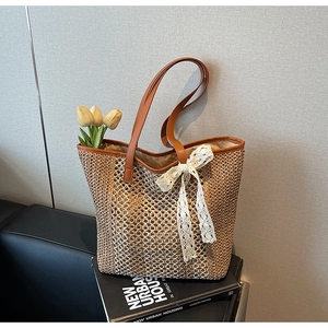 Détail du sac cabas en paille tressée avec anses en cuir marron et nœud en dentelle blanche